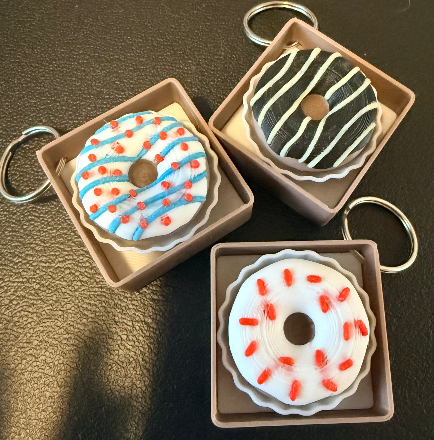 Three donut-shaped keychains in cardboard boxes on a dark surface