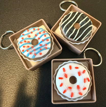 Three donut-shaped keychains in cardboard boxes on a dark surface