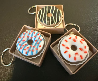 Three donut-shaped keychains in decorative boxes on a dark surface